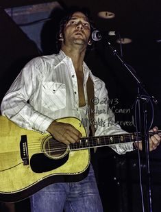 a man holding a guitar while standing in front of a microphone