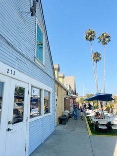 people sitting at tables in front of a building with palm trees on the other side