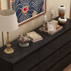 a black dresser topped with books and vases next to a painting on the wall