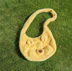 a teddy bear bag laying on the grass with it's head hanging out and eyes closed