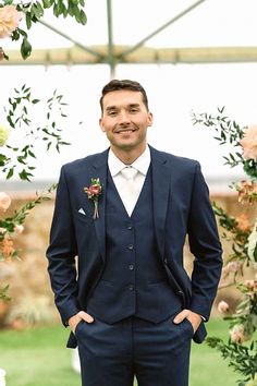 a man in a suit and tie standing under a flower covered arch with roses on it