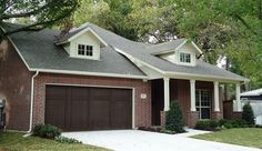 a brick house with two car garages in front of it and trees around the driveway