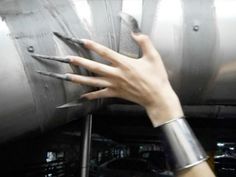 a woman's hand holding onto the side of a metal object with nails on it