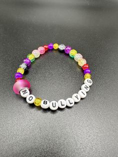 Theme: Kindness Annie's design! This bracelet features small and large multicolored beads. It has a light and dark pink closer bead. It has white letter beads that read "No Bullying".  8.5" around, stretchy. Disclaimer: This item was created by Annie. It is entirely possible for there to be spelling or other errors as a result. Any imperfections detected during the listing process have been deliberately ignored. Pink Beaded Novelty Friendship Bracelets, Novelty Pink Friendship Bracelets As Gift, Podcasts Ideas, Pink Novelty Beaded Bracelets, Novelty Letter Beads Wristband Bracelet, Pink Flower-shaped Bracelet With Letter Beads, White Letters, Letter Beads, Dark Pink