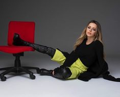 a woman sitting on the floor next to a red chair with her legs crossed and wearing black boots