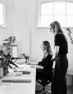 two women in black and white working at desks with plants on the windowsill