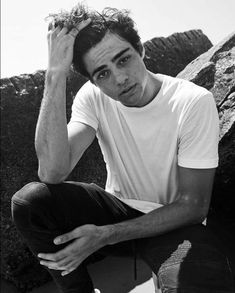 a young man sitting on top of a rock next to a pile of rocks with his hands in his hair