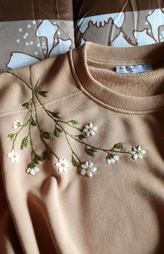 a sweater with white flowers on it laying on a bed next to pillows and blankets