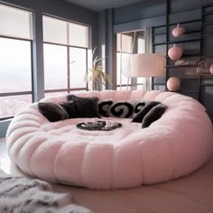 a pink dog bed sitting on top of a wooden floor in front of large windows