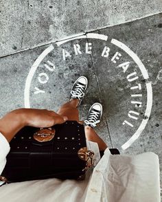 a woman sitting on the ground with her legs crossed and holding a black handbag