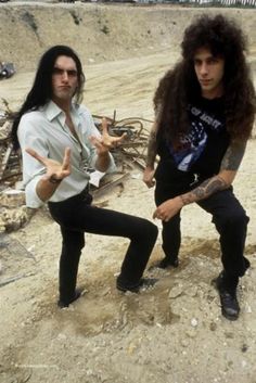 two men standing next to each other on top of a dirt covered ground with their hands in the air