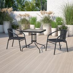 two chairs and a table on a deck with potted plants in the back ground