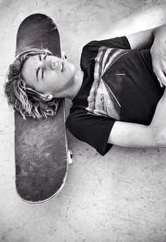 a woman laying on the ground next to a skateboard with her head resting on it