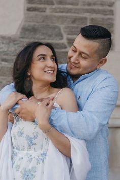 a man and woman embracing each other in front of a stone wall