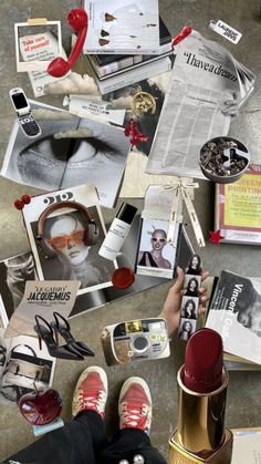 a person's feet on the ground surrounded by assorted items and magazines, including red shoes