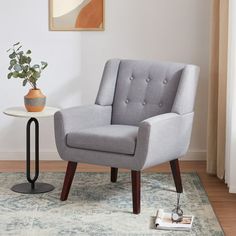 a gray chair sitting on top of a rug next to a table with a potted plant