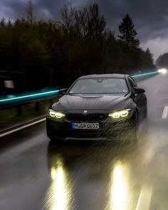 a black car driving down a wet road at night with headlights shining on the cars headlight