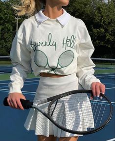 a woman holding a tennis racquet on top of a tennis court with trees in the background