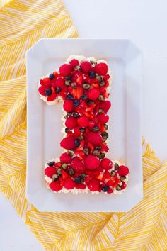 a white plate topped with a cake shaped like the number one covered in berries and nuts