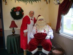 two people dressed as santa claus and mrs claus in a room with christmas wreaths on the wall