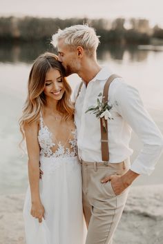 a bride and groom standing next to each other on the beach with water in the background