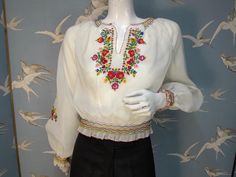 Stunning vintage hand embroidered peasant blouse dating from 1970s. Made from a semi-sheer Diolen polyester fabric, it has a beautiful embroidered floral design in primary colours on the front and sleeves. It has wide puff sleeves, smocking at the neckline, waist and cuffs, and blanket stitched rolled hems. It fastens at the side with silver poppers. Labelled size 38, would fit a UK 8/ 10. Measures a loose fitting 40" bust. Waist 24" stretching to 28". Length 18.5" from shoulder to hem. In excel Traditional Spring Blouse With Machine Embroidery, Traditional Spring Peasant Top With Embroidered Neckline, Fitted Traditional Embroidered Peasant Top, Spring Fitted Blouse With Embroidered Border, Fitted Blouse With Embroidered Border For Spring, Spring Vintage Blouse With Intricate Embroidery, Vintage Blouse With Intricate Embroidery For Spring, Spring Peasant Blouse With Embroidered Border, Vintage Blouse With Embroidered Sleeves For Spring