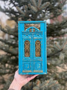 a person holding up a small blue book in front of a tree with gold designs on it