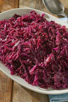 a white bowl filled with red cabbage on top of a wooden table next to a spoon