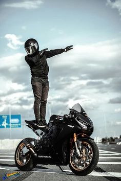 a man standing on the back of a motorcycle with his arms outstretched in front of him