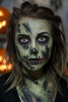 a woman with makeup painted to look like a cat is looking at the camera while she has her face painted green and black