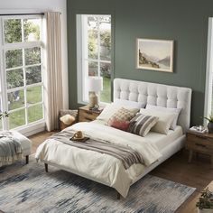 a bedroom with green walls, white bedding and rugs on the hardwood floor