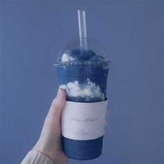 a person holding up a cup with blue liquid in it and clouds on the side