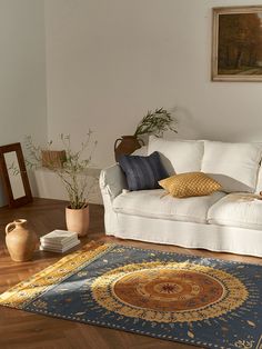 a living room with a white couch and blue rug on the wooden floor next to a potted plant