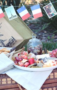 a plate of fruit and cheese on a picnic table with french flags in the background