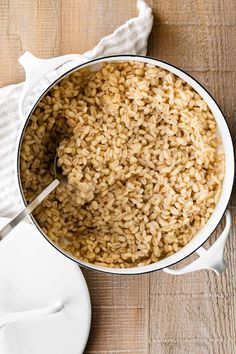 a large pot filled with brown rice on top of a wooden table next to a white plate