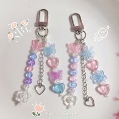 three key chains with hearts and butterflies attached to each other on a white plate next to pink flowers