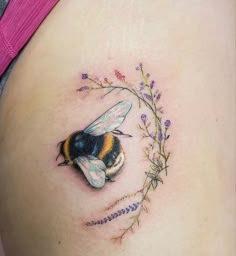 a woman's stomach with a bee and flowers tattoo on the side of her belly