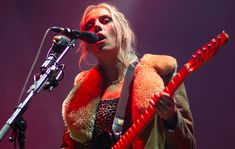 a woman with blonde hair holding a guitar and singing into a microphone at a concert