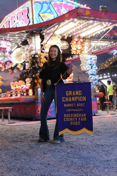 a woman holding a sign in front of a carnival