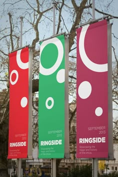 three banners are hanging on poles in front of a tree