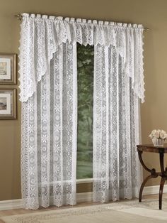 a window with white lace curtains hanging on the side of it and a table in front of