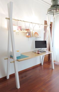 a desk with a computer on it in front of a white wall and wooden floors