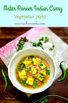 a white bowl filled with vegetable soup on top of a wooden table next to green peppers