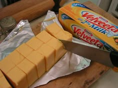 a block of cheese is cut into cubes on a cutting board with a knife