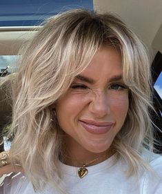 a close up of a person in a car wearing a white shirt and blonde hair