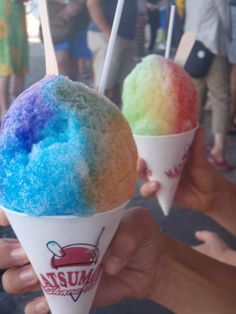 two ice cream cones with different colored toppings on them, being held by people