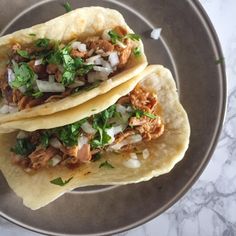 two tacos are sitting on a plate with onions and cilantros in it