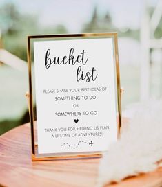 a sign that says bucket list sitting on top of a wooden table next to a white feather