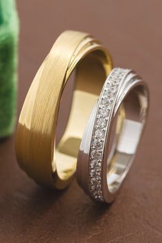 two gold and silver wedding bands with diamonds on them, sitting next to each other