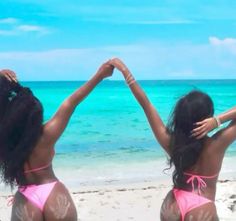 two women in bikinis standing on the beach with their arms up to each other